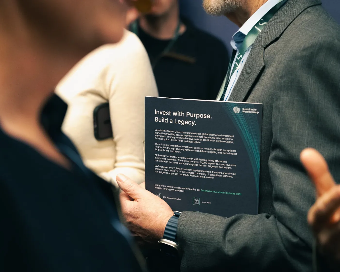 Investors reading a Sustainable Wealth Group brochure at an investment event
